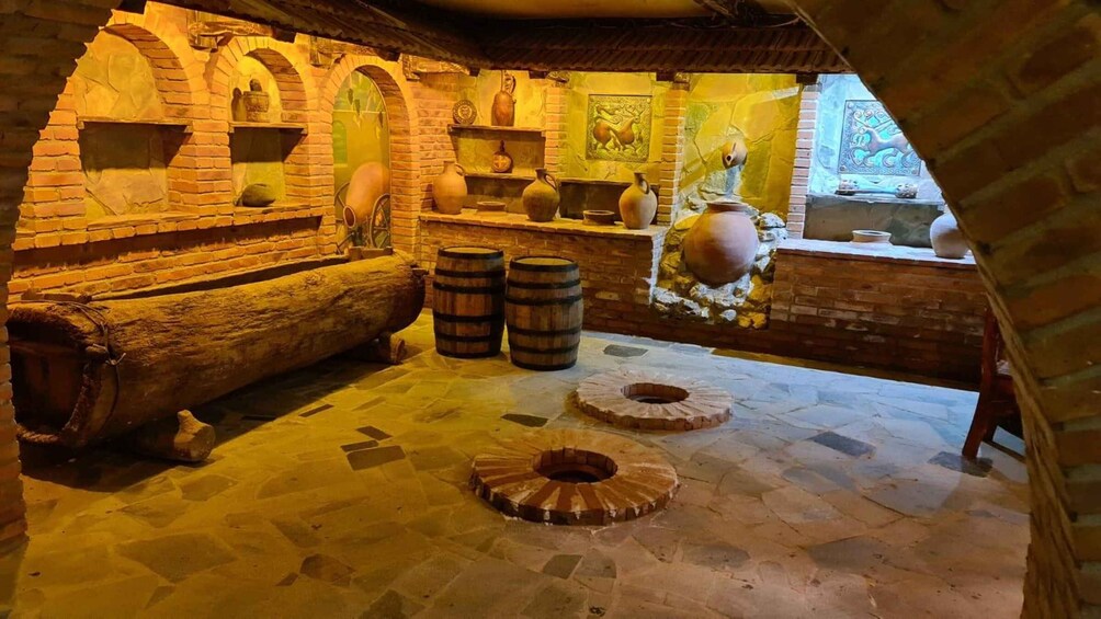 A rustic interior with stone walls, wooden barrels, and traditional pottery. 3