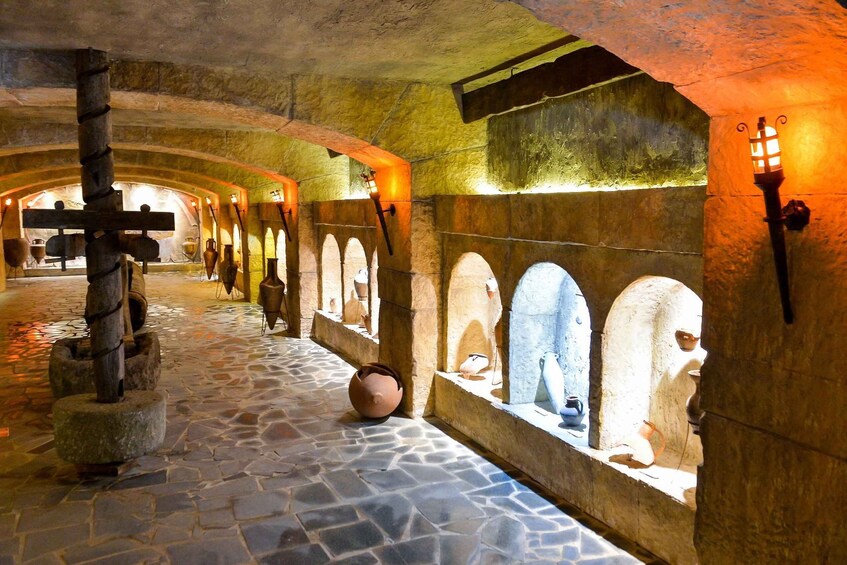 A stone-walled corridor with arched niches, a large cross, and a stone mill. 1