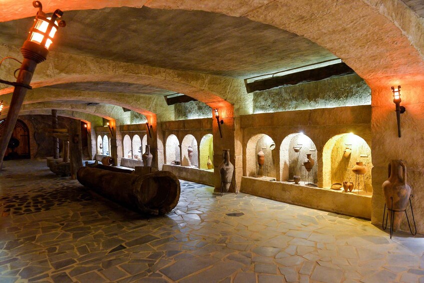 An underground stone corridor with arched ceilings, stone flooring, and pottery displayed in niches. 2