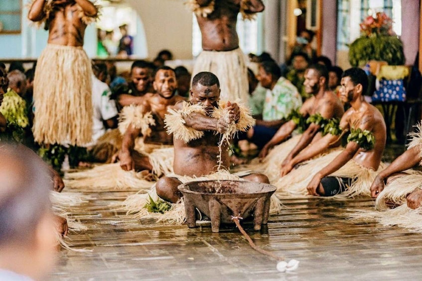 A group of people in traditional attire sitting on the floor, engaged in a ritual with a central pot. 4