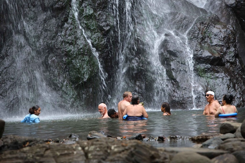 A group of people in a natural water setting with a waterfall in the background. 3