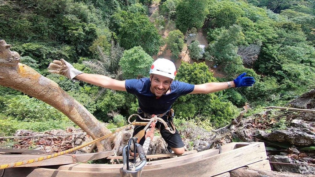 A person rappelling down a rocky cliff with a rope, surrounded by dense forest. 1