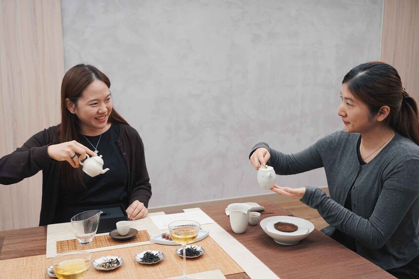Two individuals at a table with teapots, cups, and tea leaves. 3