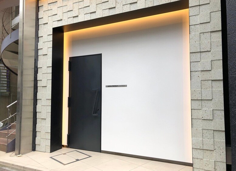 A modern building entrance with a black door, a sign reading 'JAPAN PREMIUM LOUNGE,' and a glass staircase to the left. 2
