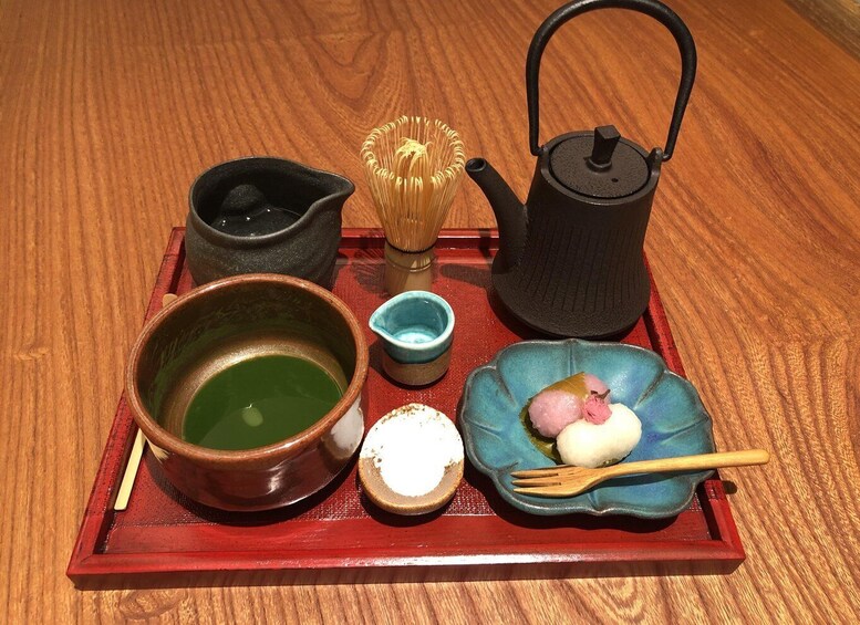 A traditional Japanese tea set on a tray, including a teapot, cups, and a whisk. 1