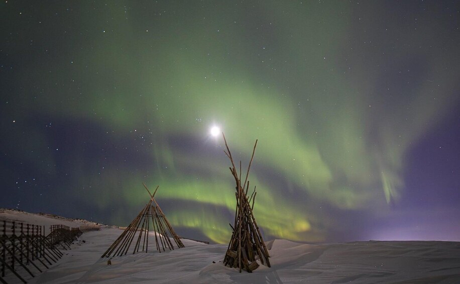 A snowy landscape with two wooden structures and the Northern Lights in the background. 3