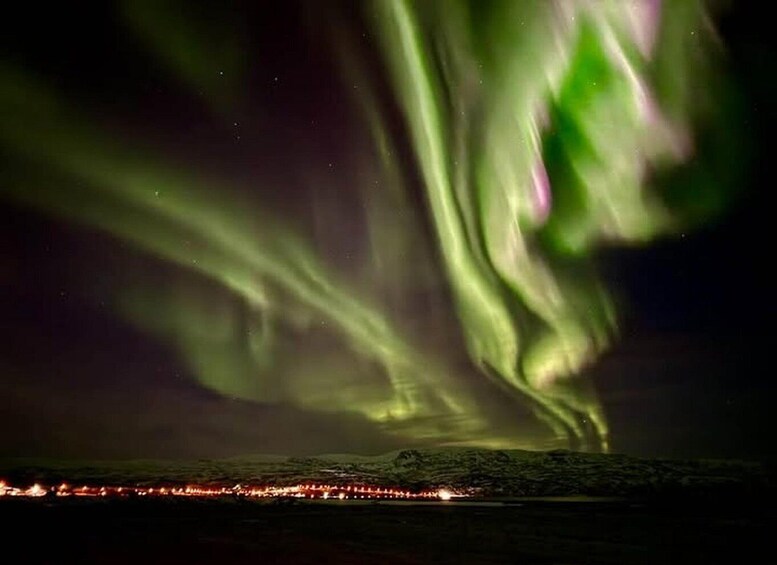 The Northern Lights over a coastal landscape with city lights in the distance. 5