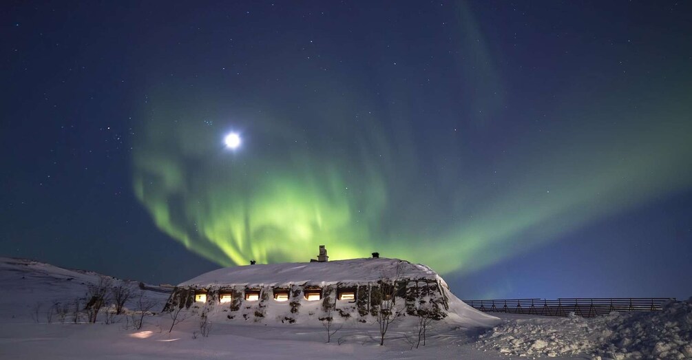 A snow-covered hill with a building at the top, under a night sky with the aurora borealis. 4