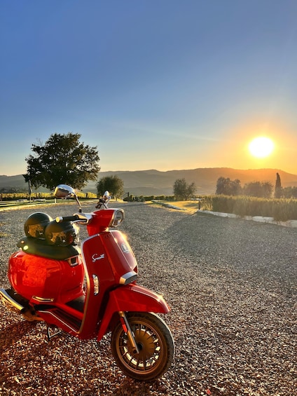 A red scooter parked on a gravel path with a sunset in the background. 3