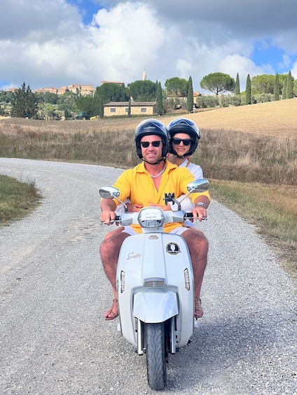 A couple on a white scooter on a gravel road with a rural landscape in the background. 4