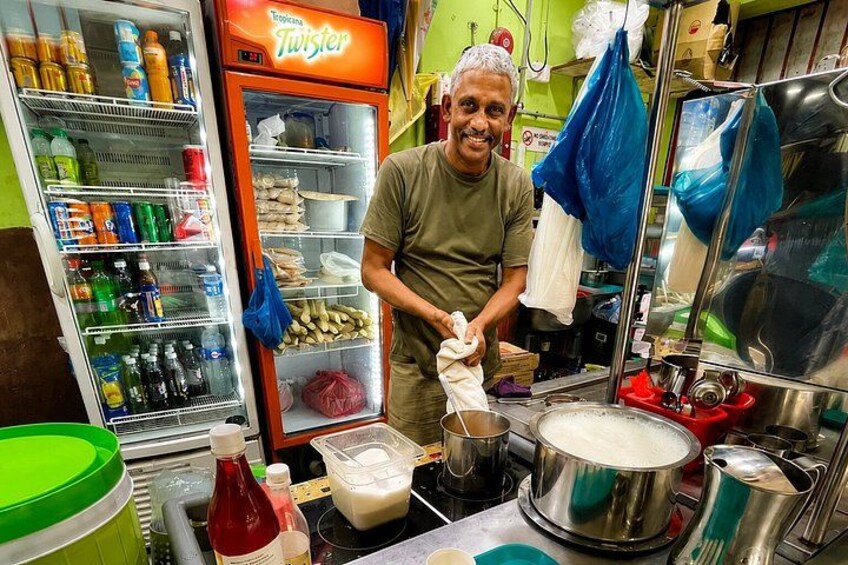 A person preparing food in a kitchen with a refrigerator stocked with beverages and a large pot on the counter. 5
