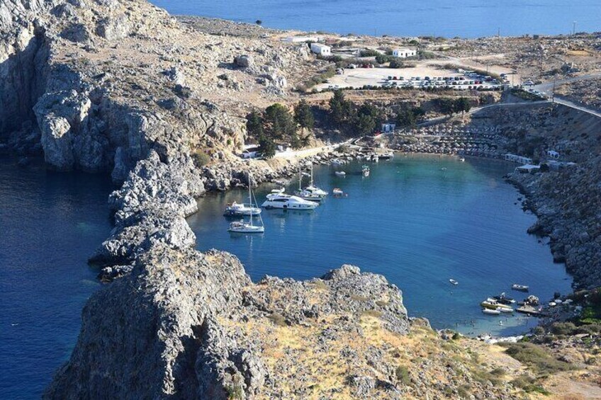A rocky coastline with boats anchored in a bay, a bridge, and buildings in the distance. 4