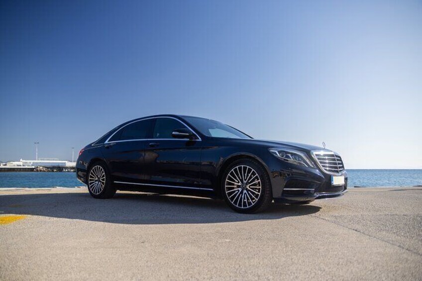 A black luxury sedan parked on a coastal road with a clear sky and ocean in the background. 2