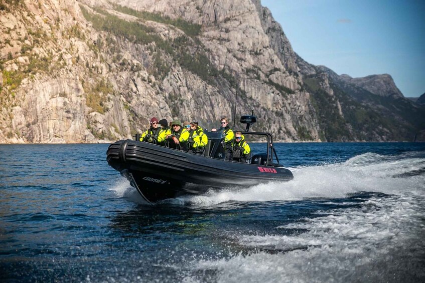 A boat with people wearing bright yellow life jackets on a body of water with rocky cliffs in the background. 2