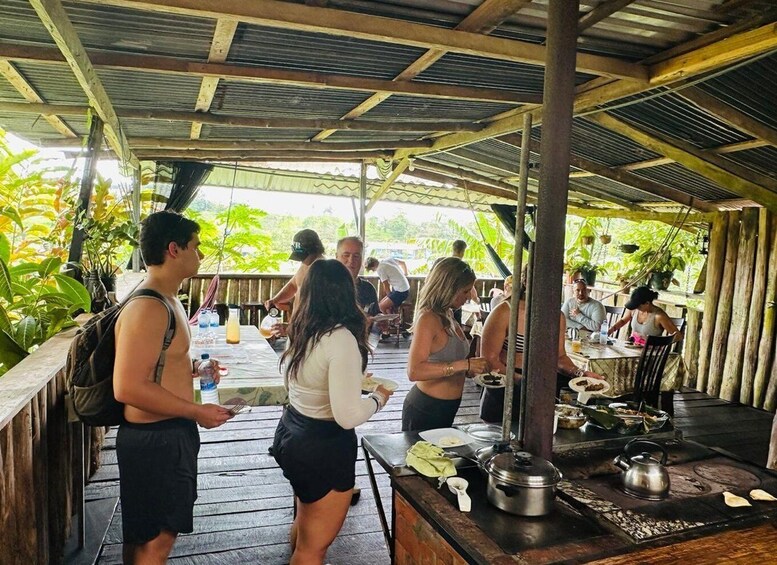 A covered outdoor dining area with people eating and socializing, surrounded by lush greenery. 2