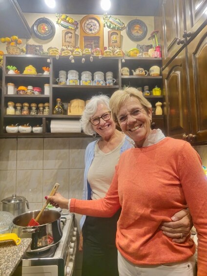 Two people in a kitchen with shelves of kitchenware and a pot on the stove. 2