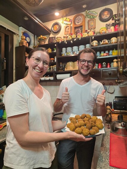 Two people in a kitchen holding a tray of food. 1