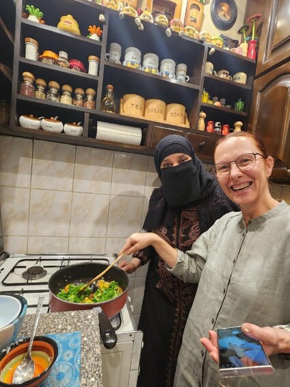Two people cooking in a kitchen with various jars and kitchenware on shelves. 5