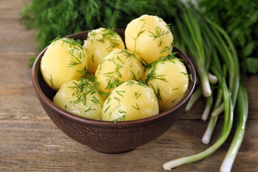 A bowl of boiled potatoes garnished with dill, with green onions and parsley in the background. 3