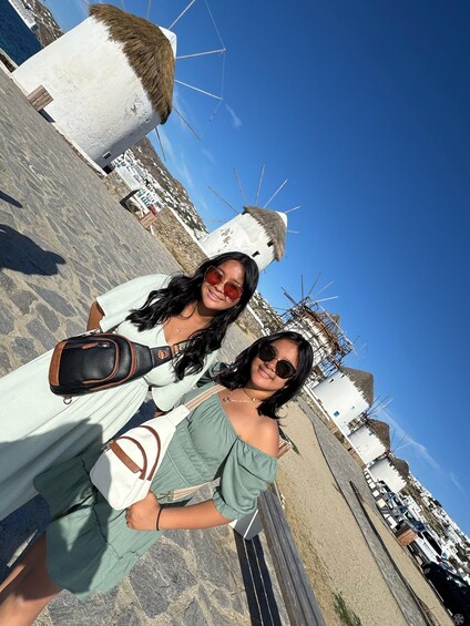Two people standing in front of windmills with thatched roofs, on a sunny day. 3