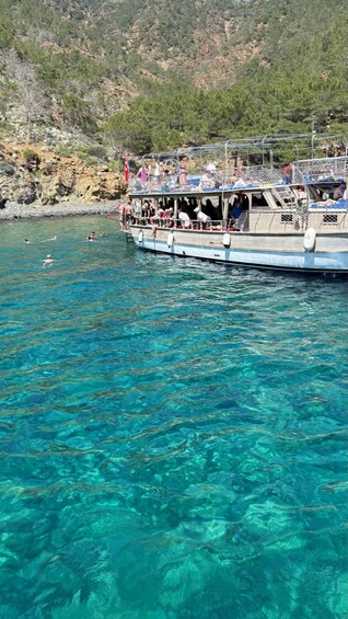 A boat with people on a clear blue sea, rocky hills in the background. 5