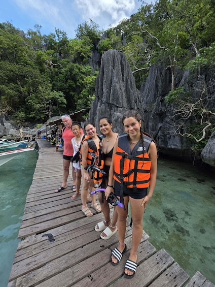 A group of people on a wooden dock with clear water and rocky cliffs in the background. 4