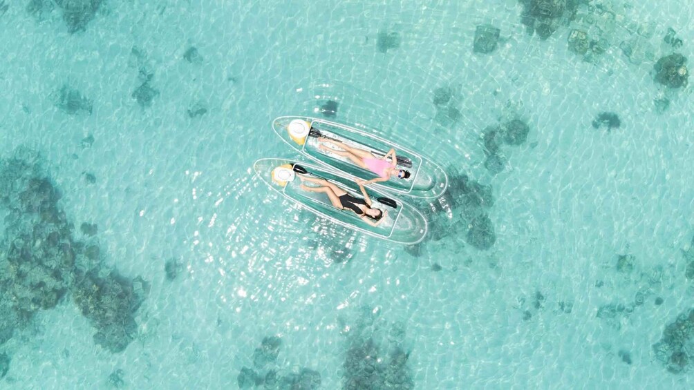 Three people floating on clear blue water using inflatable tubes. 1