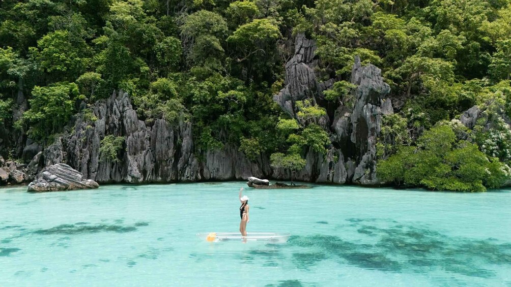 A person paddleboarding in turquoise waters with a backdrop of rocky cliffs and dense greenery. 2