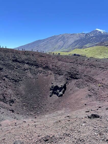 A volcanic landscape with a group of people hiking, a crater, and a mountain with snow-capped peak. 4