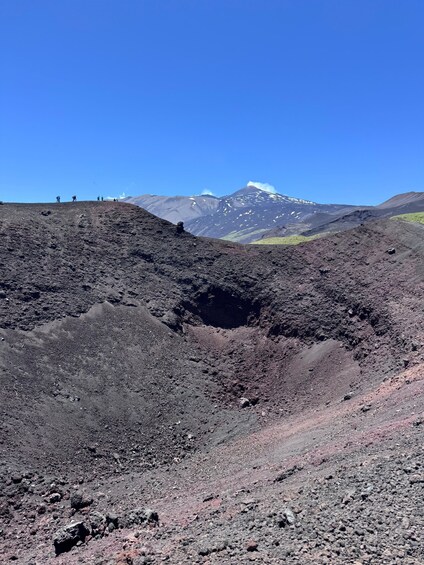 A volcanic landscape with a crater, rocky terrain, and a mountain with snow in the background. 2