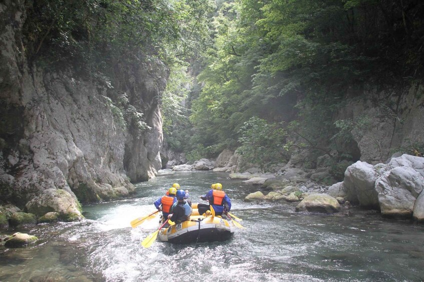 A group of people rafting down a river surrounded by rocky cliffs and dense foliage. 5