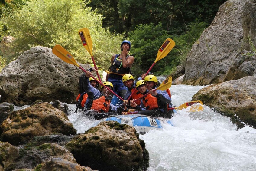 A group of people in a raft navigating a river with rapids, surrounded by rocks and greenery. 1