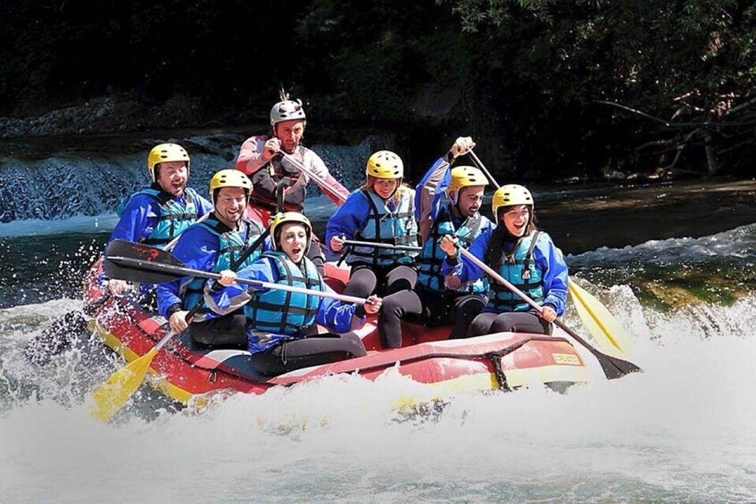A group of people in a red raft with yellow helmets, paddling on a river. 2