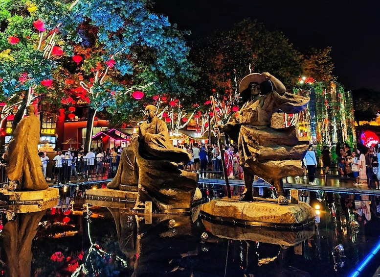 A night scene with illuminated statues of historical figures, a reflective water surface, and traditional architecture in the background. 2