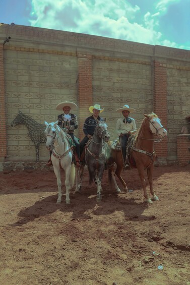Three people on horseback in front of a brick wall. 3