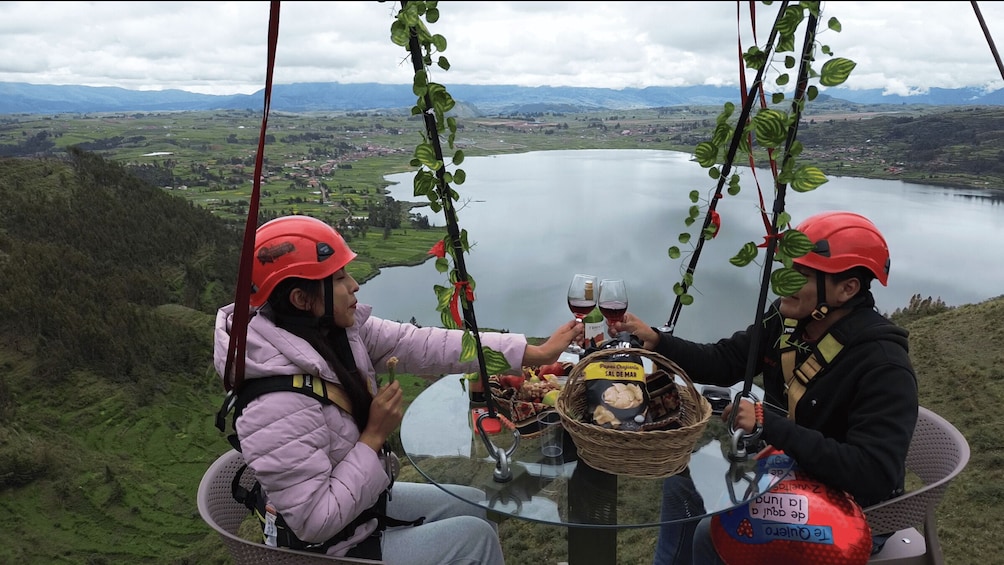 Two people in a wicker basket at a high vantage point overlooking a lake and mountains. 1