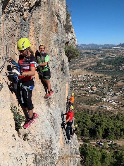 Climbers on a steep rock face with a valley and buildings in the background. 2