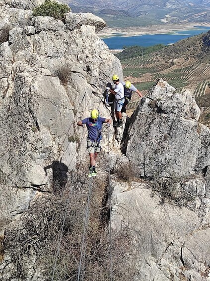 Climbers ascending a rocky mountain with a lake in the background. 4