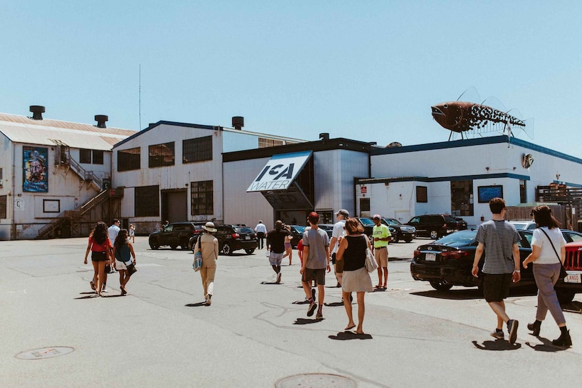 A parking lot with people walking, a building with 'ICA WATER' sign, and a large fish sculpture on the roof. 2