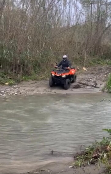 A person riding an orange ATV on a muddy path beside a river. 2