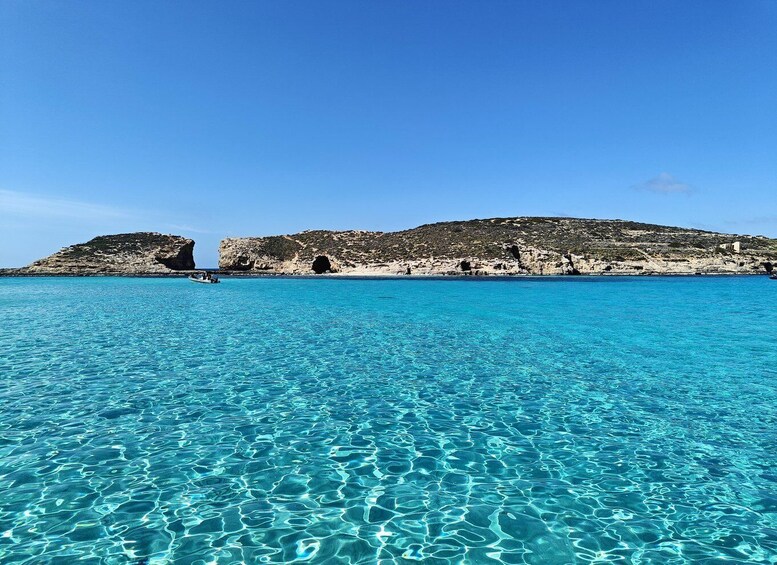 A clear blue sea with rocky outcrops and a boat in the distance. 2