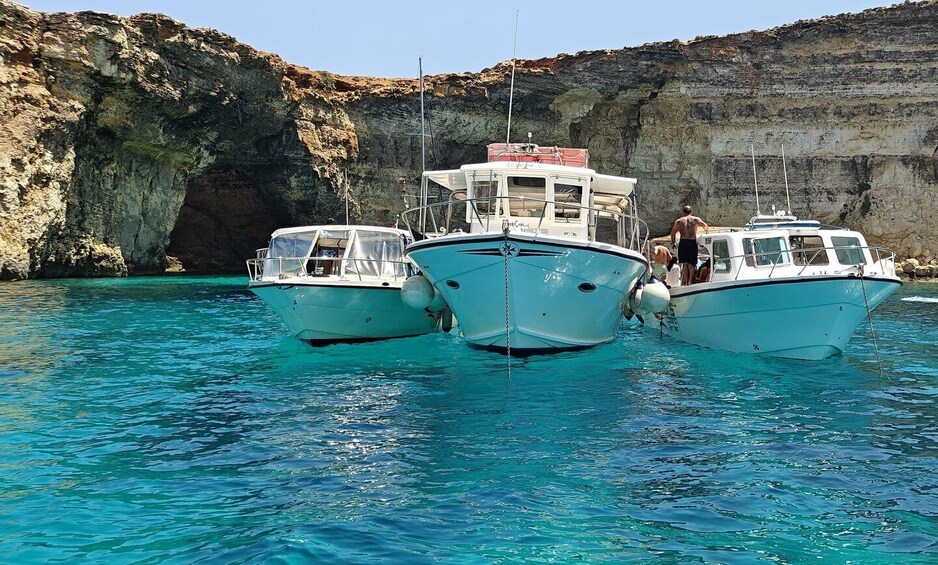 Two boats anchored near a rocky cliff with clear blue water. 3