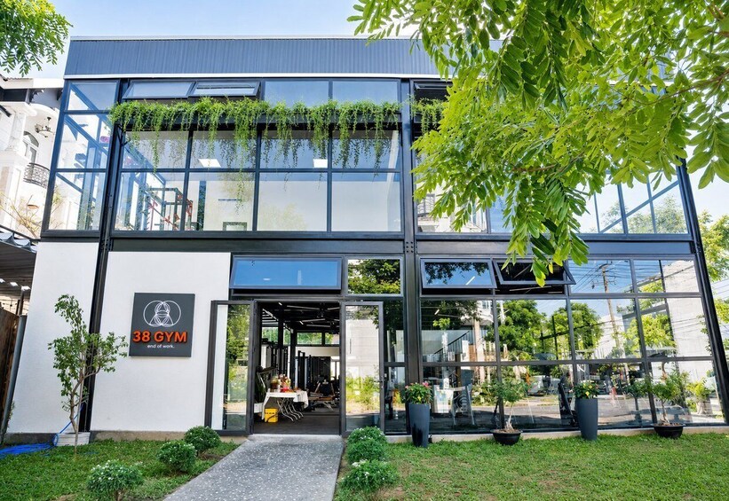 Moderni rakennus, jossa on suuret ikkunat, kyltti, jossa lukee ”38 Gym – työt päättyivät”, ja ruukuissa olevia kasveja maassa. 4