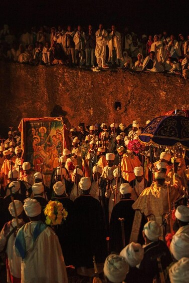 A group of people in traditional attire gathered around a religious icon, with a crowd watching from a raised platform. 1