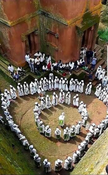 A group of people in white traditional attire arranged in concentric circles in an outdoor setting. 3