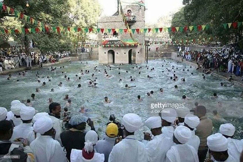 A large gathering of people in a natural water body, possibly a river, with a stone structure in the background. 4