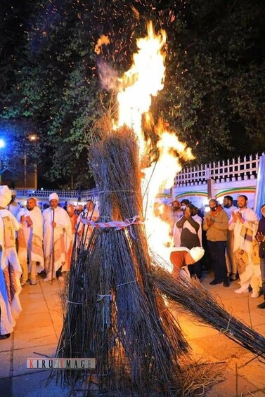 A fire ritual with a bundle of sticks burning, surrounded by onlookers. 3