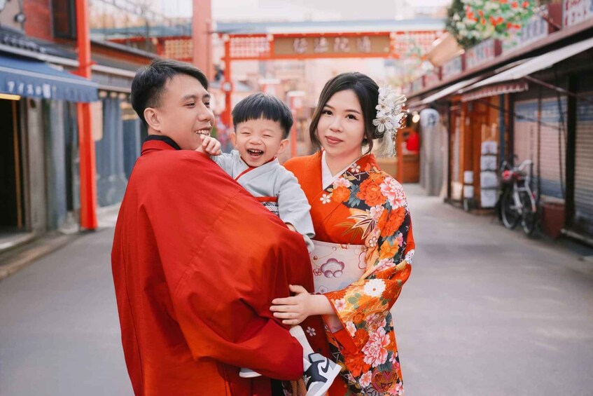 A person in a red garment holding a child, another person in a floral kimono, and a traditional Japanese torii gate in the background. 5