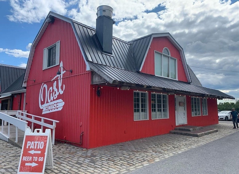 A red building with a sign that reads 'Oast House' and a sign indicating a patio and beer to go. 2