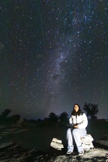 A person sitting on a wooden structure under a starry night sky. 2